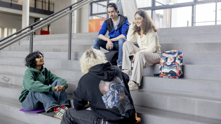 Vier Studierende im Gespräch auf der großen Treppe im Foyer der TH Köln, Campus Gummersbach. (Bild: TH Köln, Hanna Witte)
